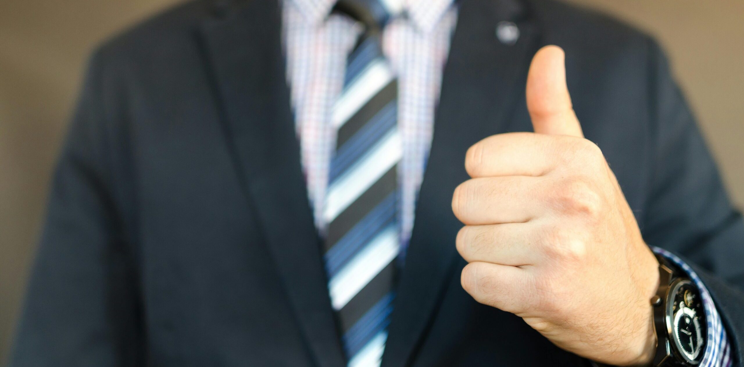 pexels-photo-653429-653429 Close-up of a businessman in a suit giving a thumbs up gesture, symbolizing success.